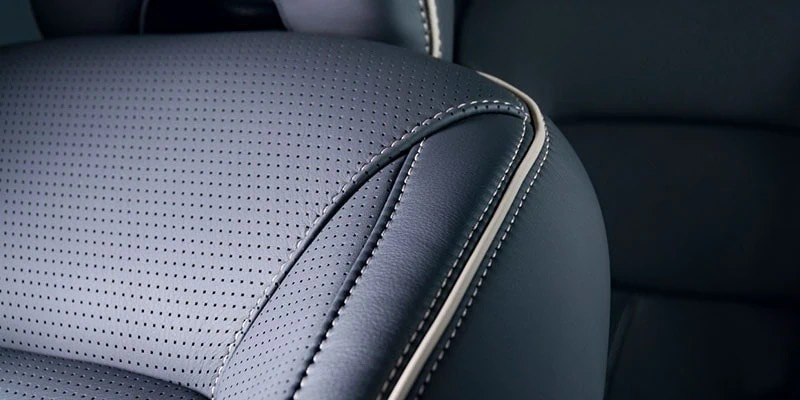 Close-up of dark perforated automotive upholstery with a stitched smooth bolster and pale piping